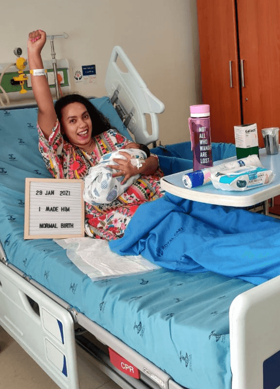Sukanya holding her newborn while resting in a hospital bed after delivery.